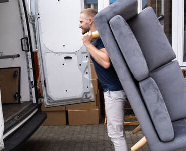 Möbellift Jena: Helfer tragen ein graues Sofa aus einem Transporter
